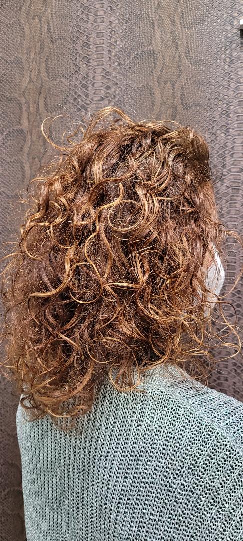 Una mujer con cabello rojo rizado lleva un suéter azul.