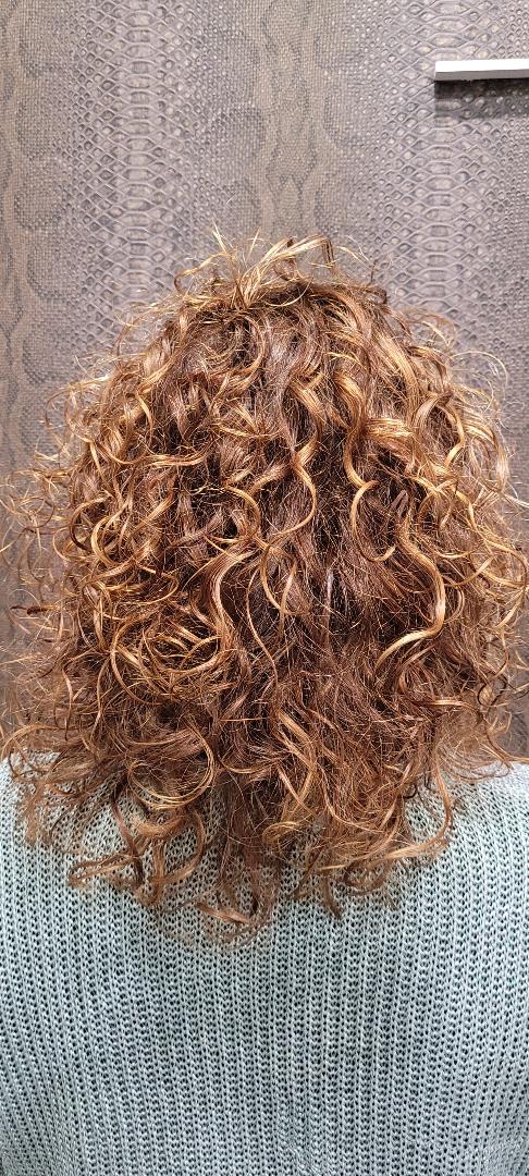Una mujer con cabello rojo rizado lleva un suéter azul.
