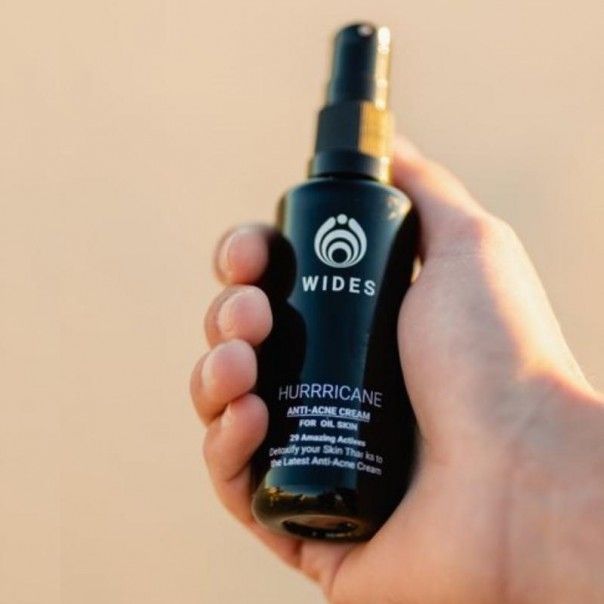Una persona sostiene una botella de crema antiacné Hurricane.
