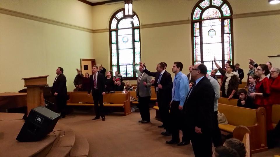 A group of people are standing in a church with their hands in the air.