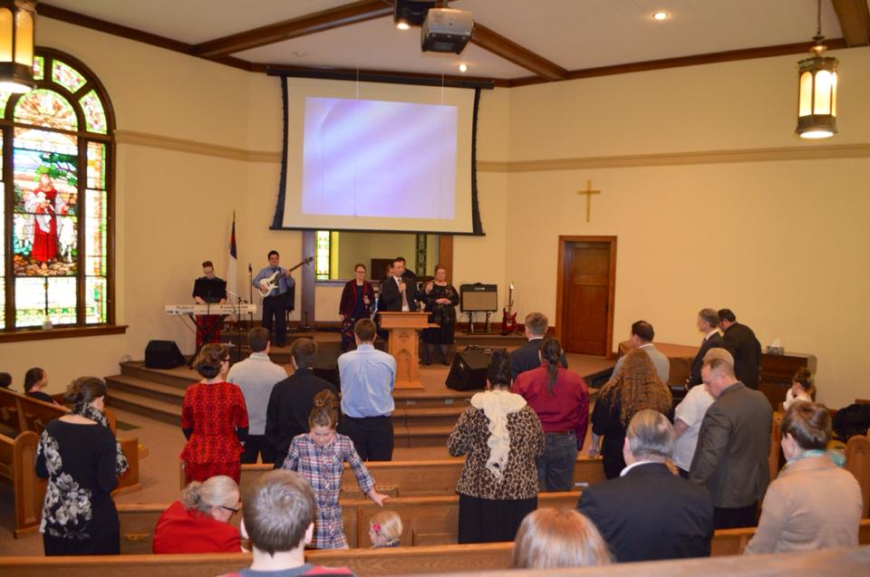 A group of people are standing in front of a projector screen in a church.