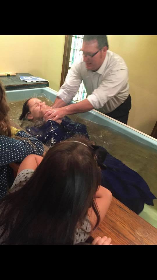 A man is baptising a woman in a pool of water.