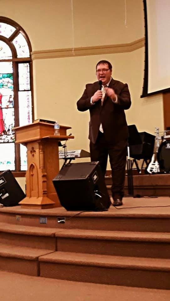 A man in a suit is giving a speech at a podium in a church.
