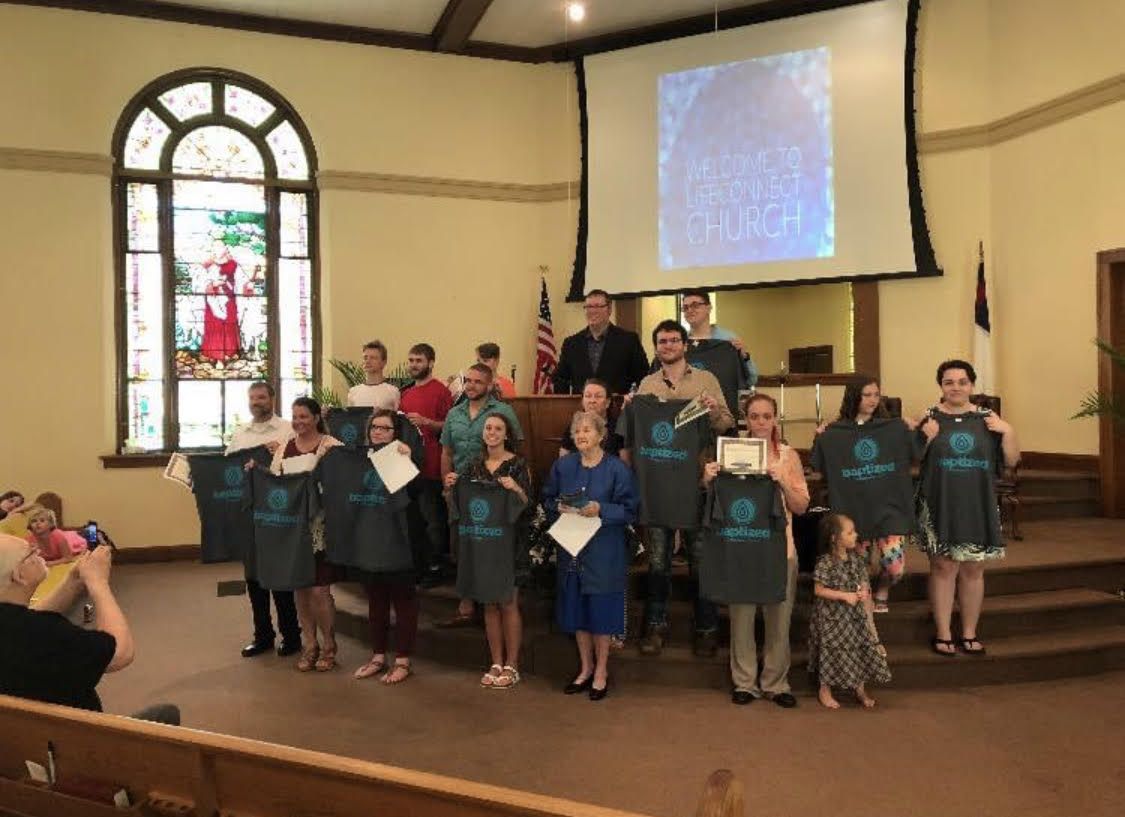 A group of people are standing in a church holding t-shirts.
