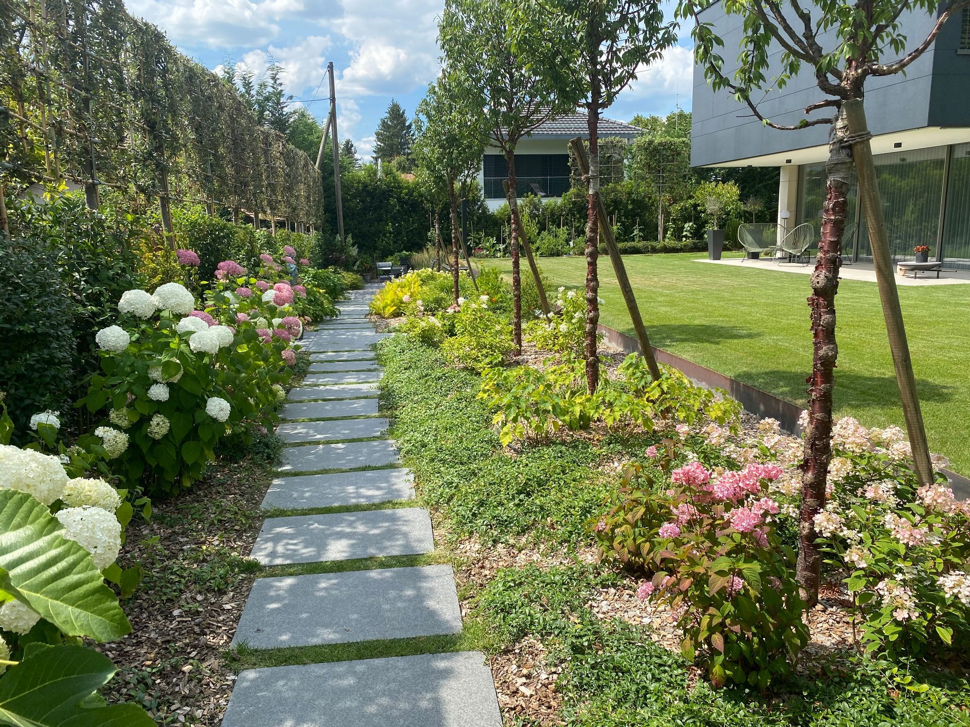 un chemin de pierre traverse un jardin rempli de fleurs et d' arbres .