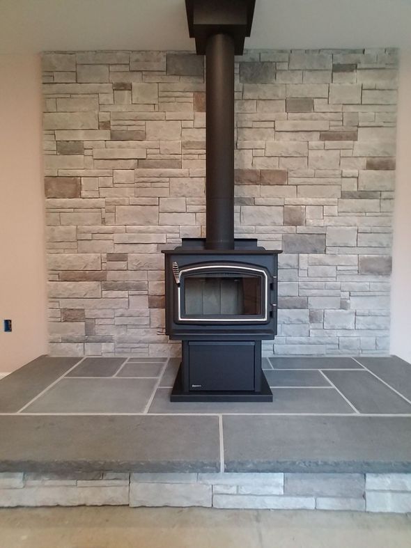 A wood stove in front of a stone wall JW Chimneys in Collegeville PA and surrounding areas.