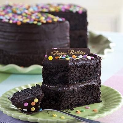 Chocolate birthday cake with colorful sprinkles and a slice on a plate.