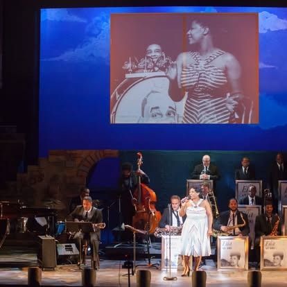 A stage performance with a singer, band, and a projection of a black and white photo of a singer.