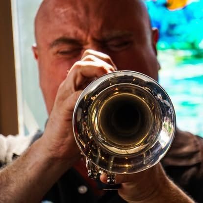 Bald man playing a trumpet, eyes closed, brass instrument close up. Blurred background.