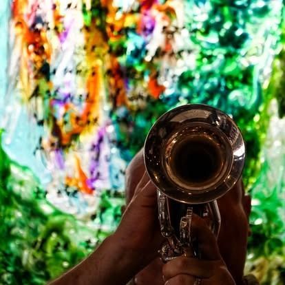 Person playing a silver trumpet, colorful abstract background.