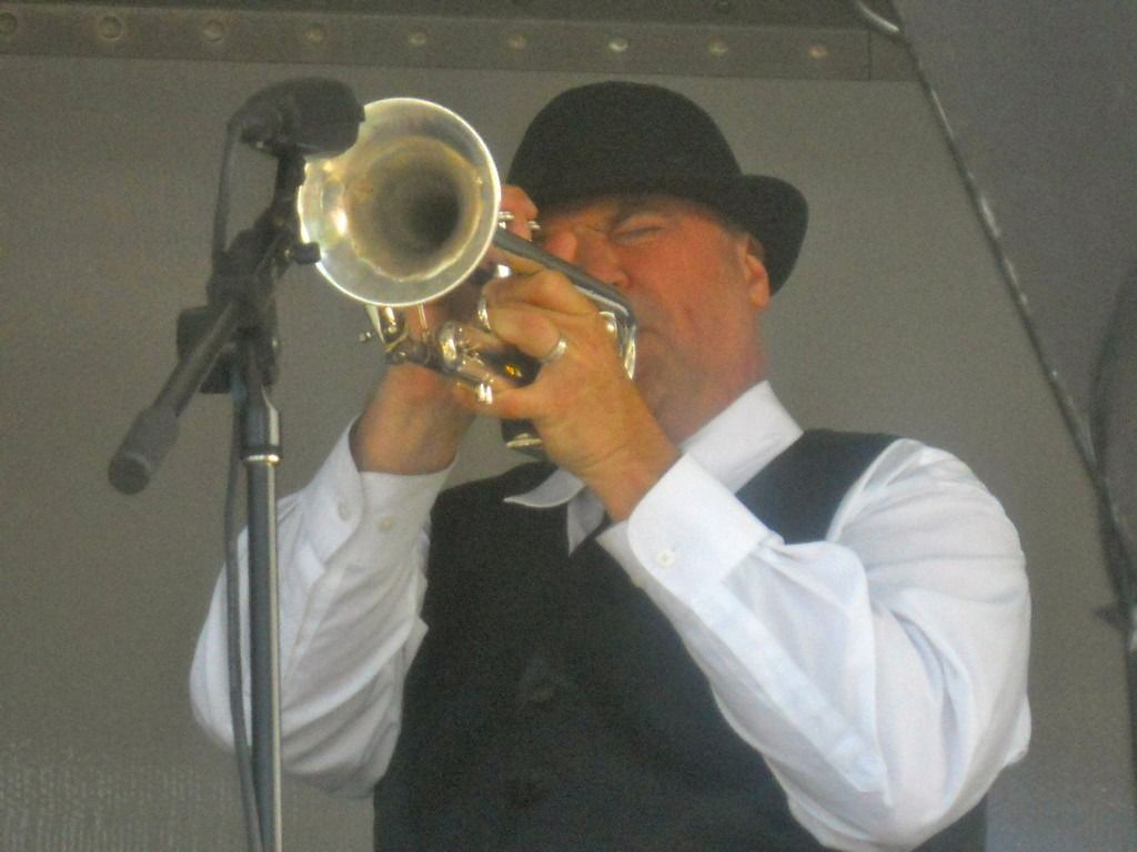 Man in bowler hat plays trumpet into a microphone.