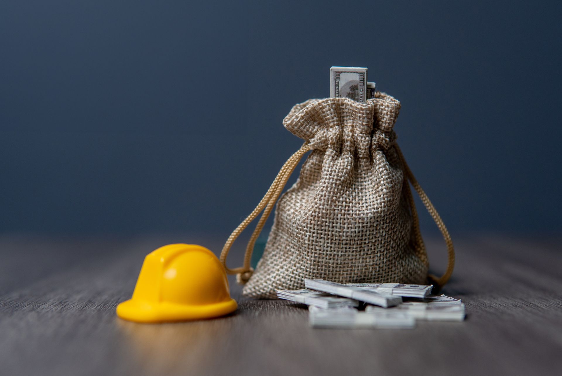 A yellow hard hat and a bag of dominoes are on a wooden table.