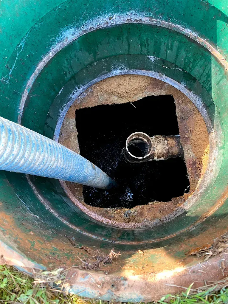 Inside view of a green septic tank with a hose inserted, dark liquid visible.