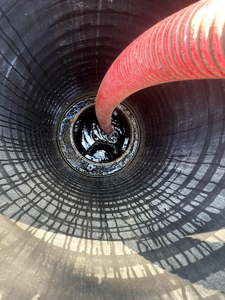 Red hose pouring dark liquid into a cylindrical tank.