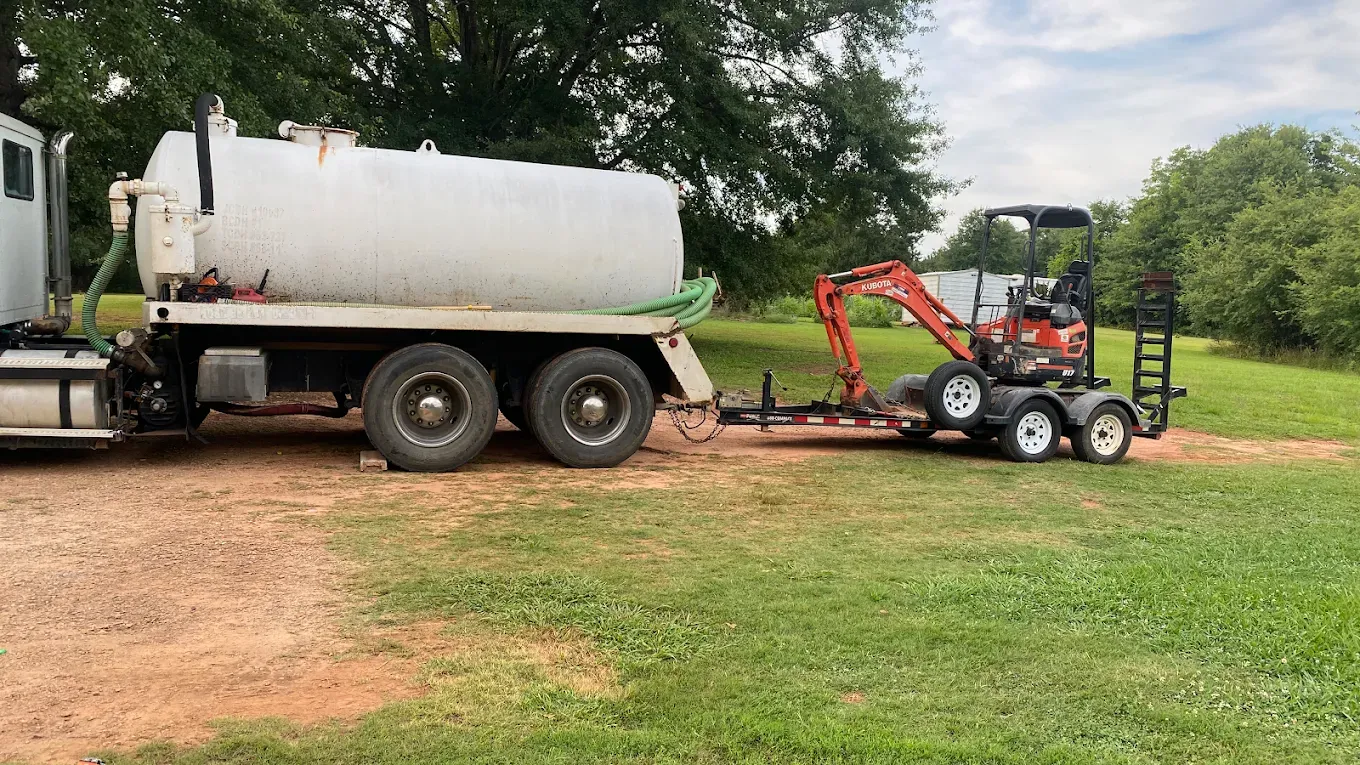 A white truck pulling a large water tank and a trailer with an excavator.