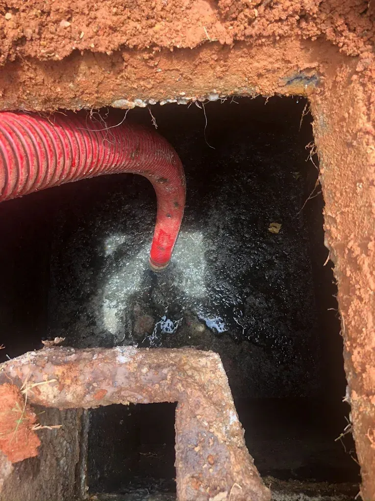 Sewer tank with black liquid, red hose, and brick frame. Tank is open, viewed from above, surrounded by dirt.