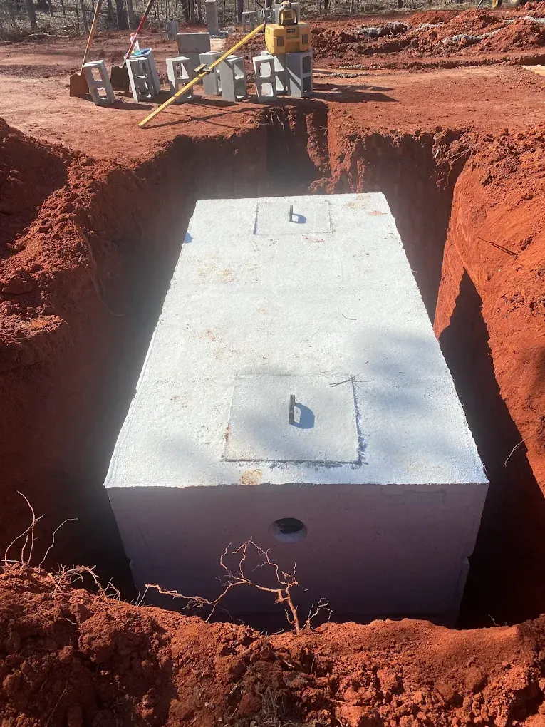 Concrete septic tank in red dirt trench, construction site.