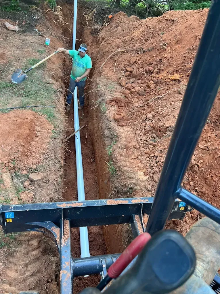 Man in trench using shovel, working on installing a pipe in a ditch. View from equipment.