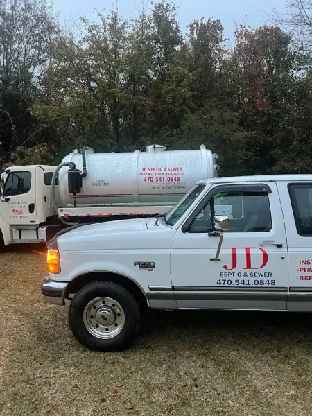 White trucks with JD Septic Service branding parked outdoors near trees.