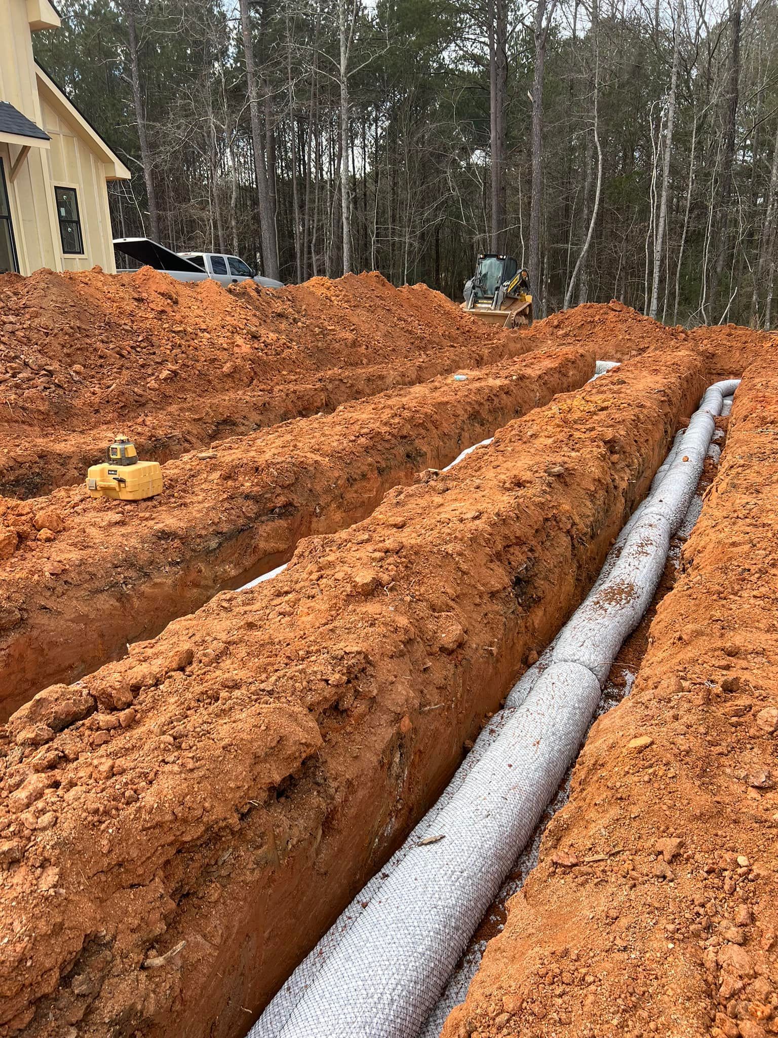 Trenches with white gravel and fabric for drainage in construction site with dirt.