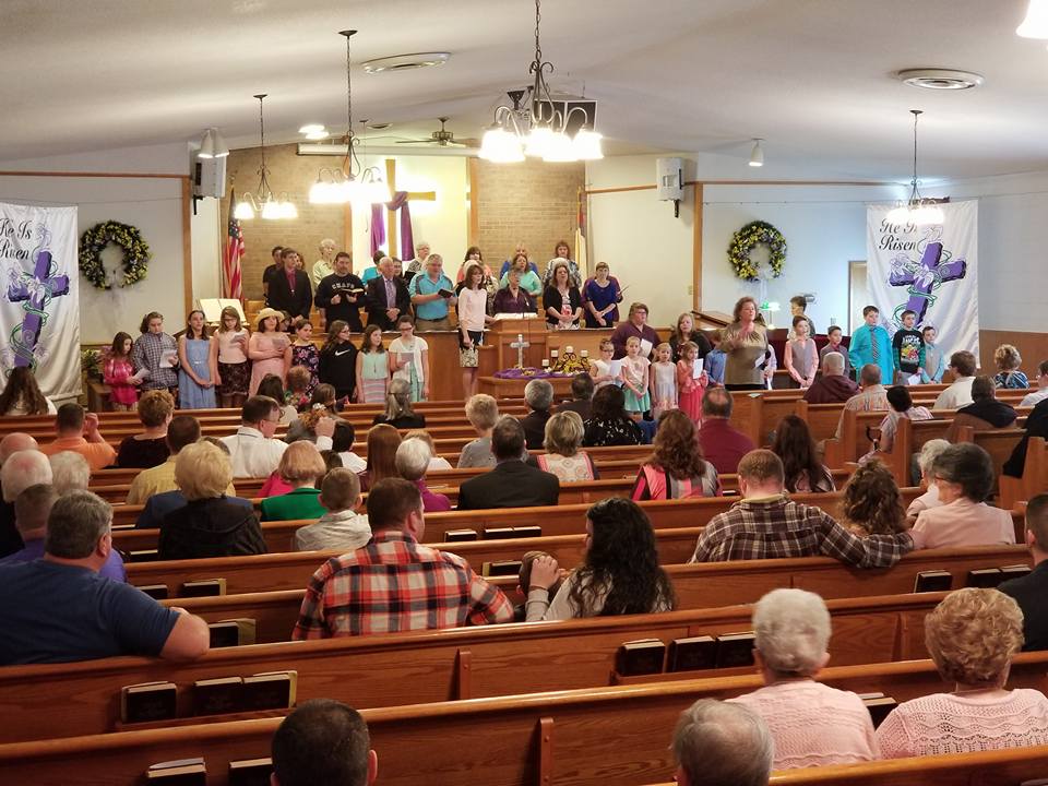 Church service with people singing and listening, purple cross decorations.
