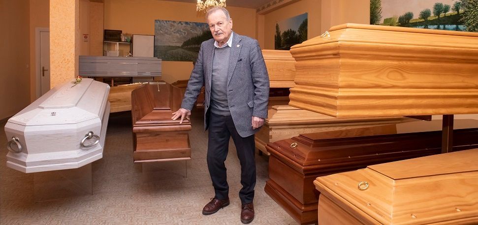 A man is standing in a room full of wooden coffins.