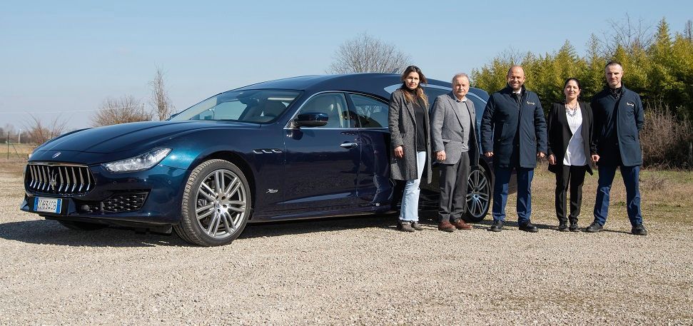 A group of people are standing in front of a blue car.