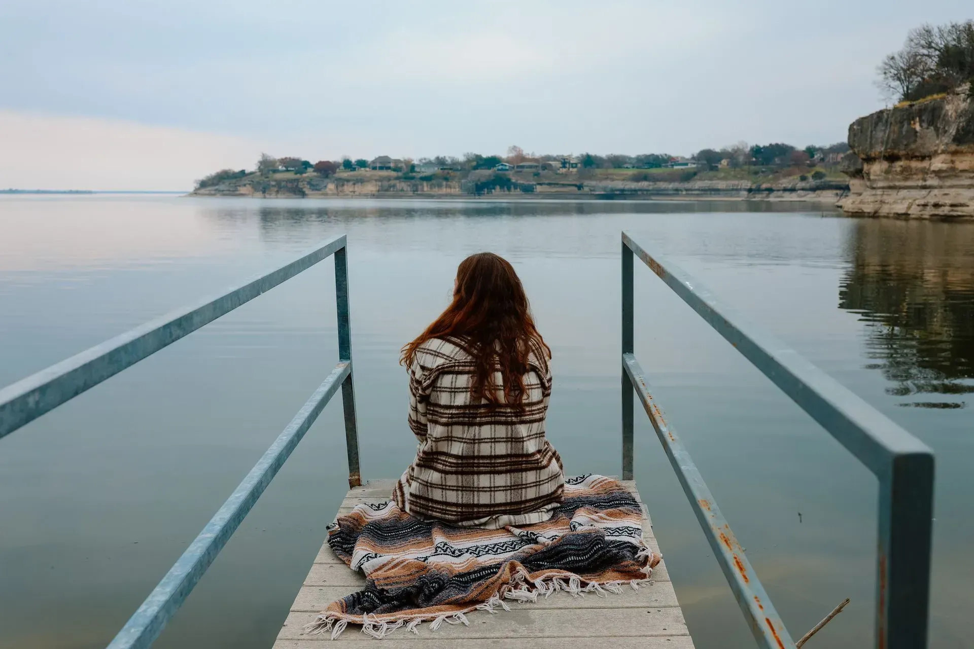 A woman is sitting on a dock overlooking a lake.