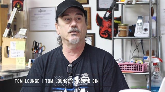 A man wearing a black hat and a black shirt says tom lounge