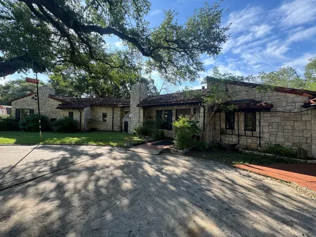 A large stone house with a driveway and trees in front of it.