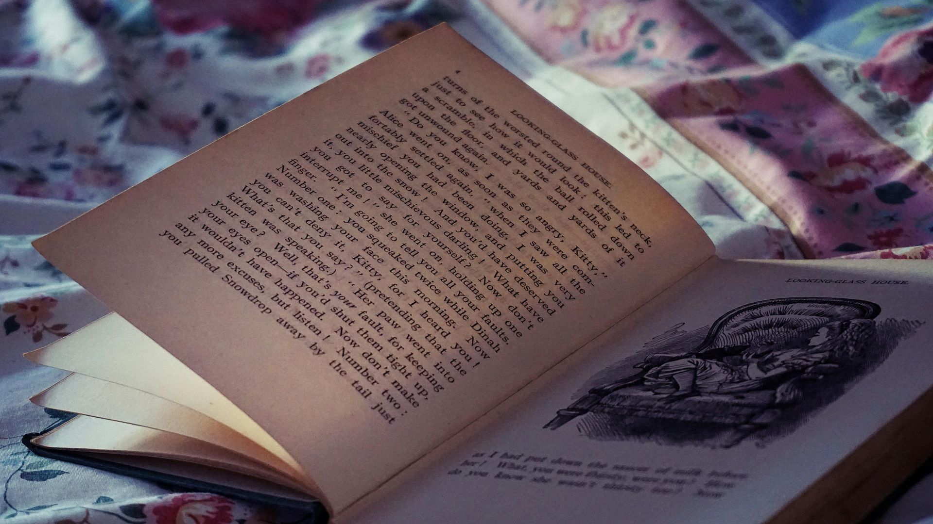 An open book is laying on a bed with a floral blanket.