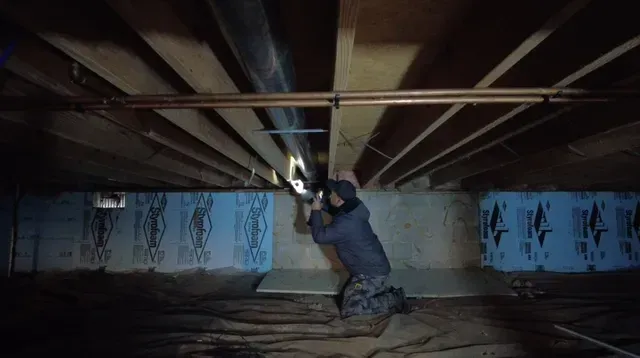 A man is working on a pipe in a basement.