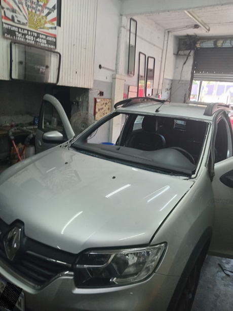 Un coche Renault plateado dentro de un taller mecánico, con el parabrisas quitado.