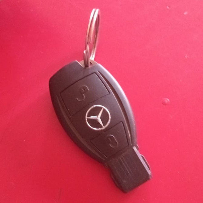 Un llavero negro de Mercedes-Benz con tres botones, sujeto a una anilla metálica sobre un fondo rojo.