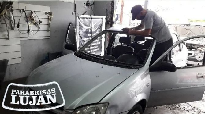 Un mecánico instala un parabrisas en un coche plateado dentro de un taller de reparación.