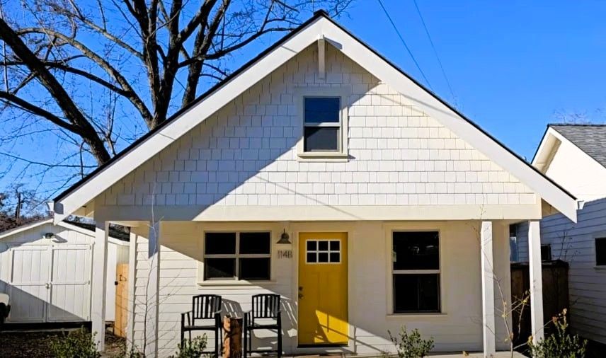 Small white ADU with yellow door and shaded porch for aging parents