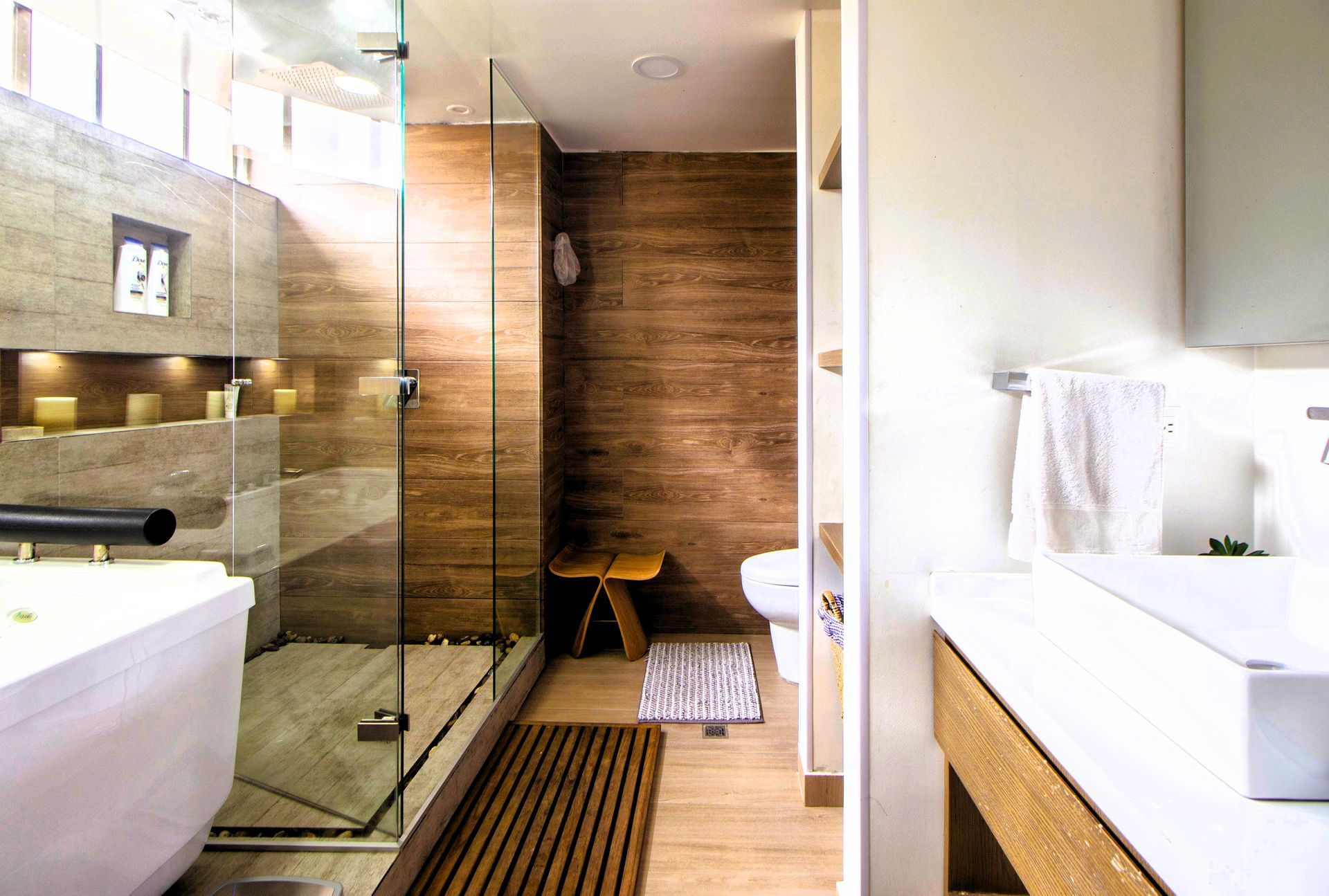 Modern bathroom with a glass shower, wooden accents, and white fixtures.