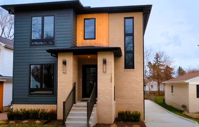 Modern two-story custom home in Michigan with dark and light brick facade, large windows, and a covered entrance.