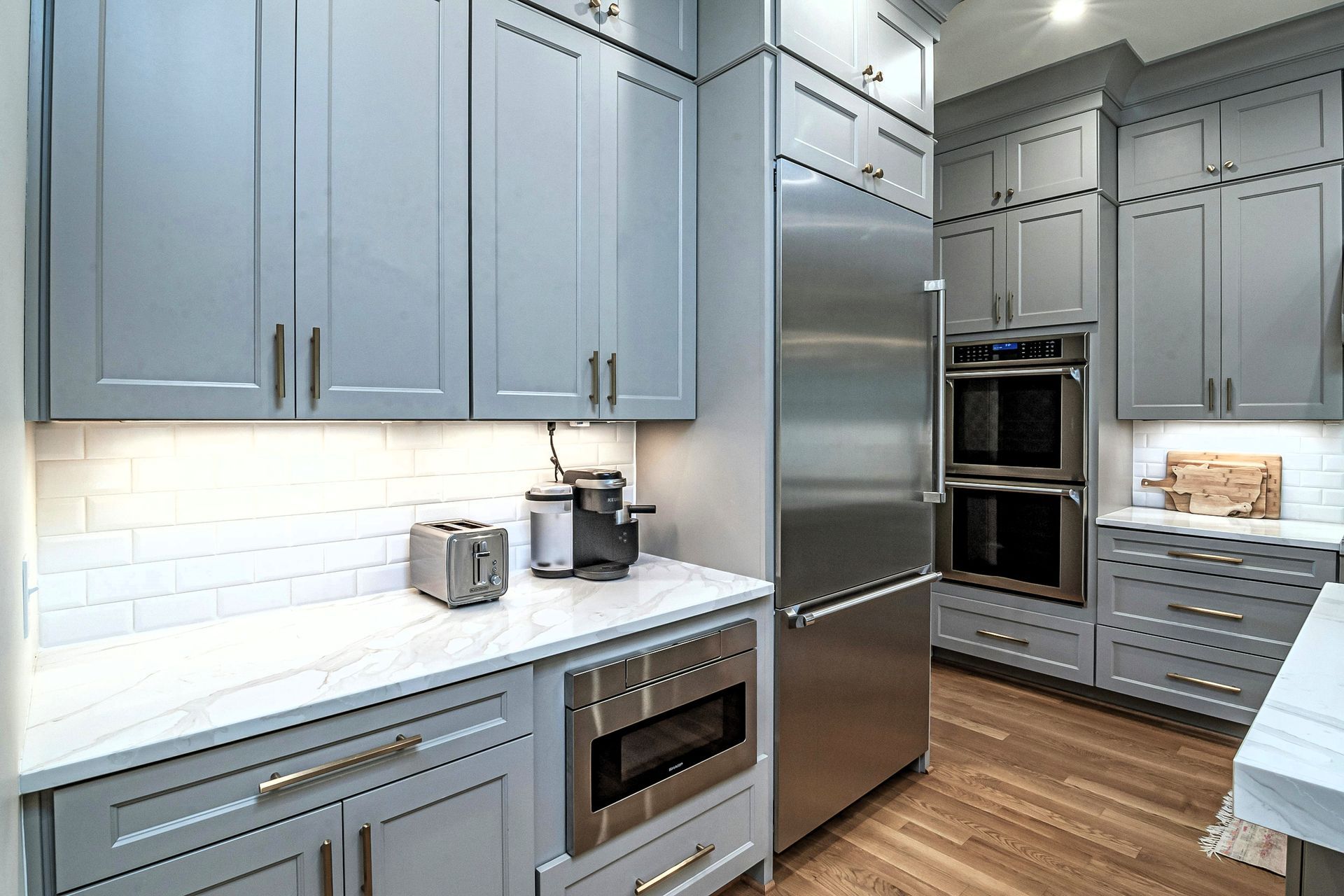 Modern kitchen with grey custom cabinets, stainless steel appliances, and white backsplash.