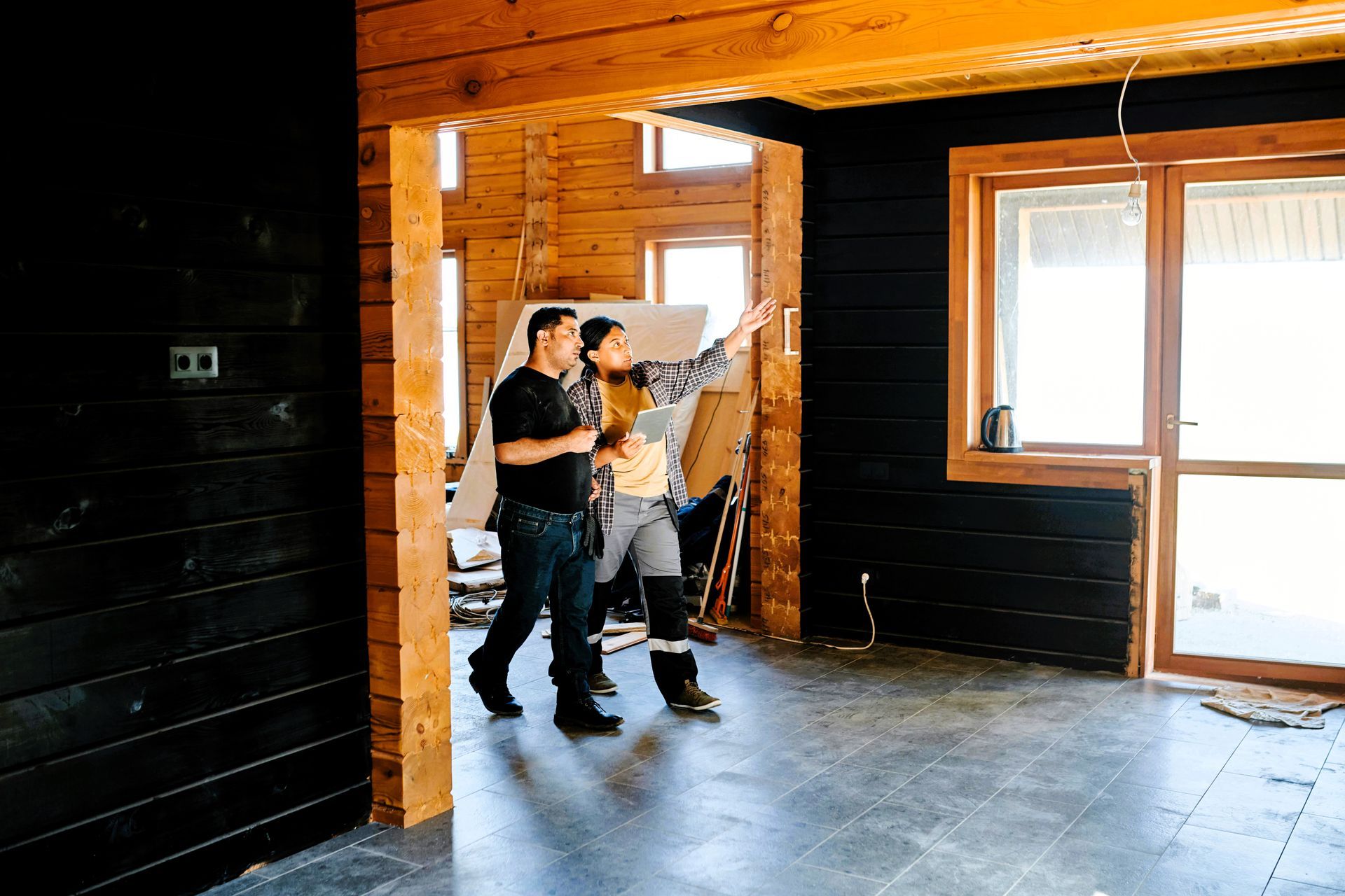 Two remodeling contractors discussing in a room under construction, one holding a clipboard.