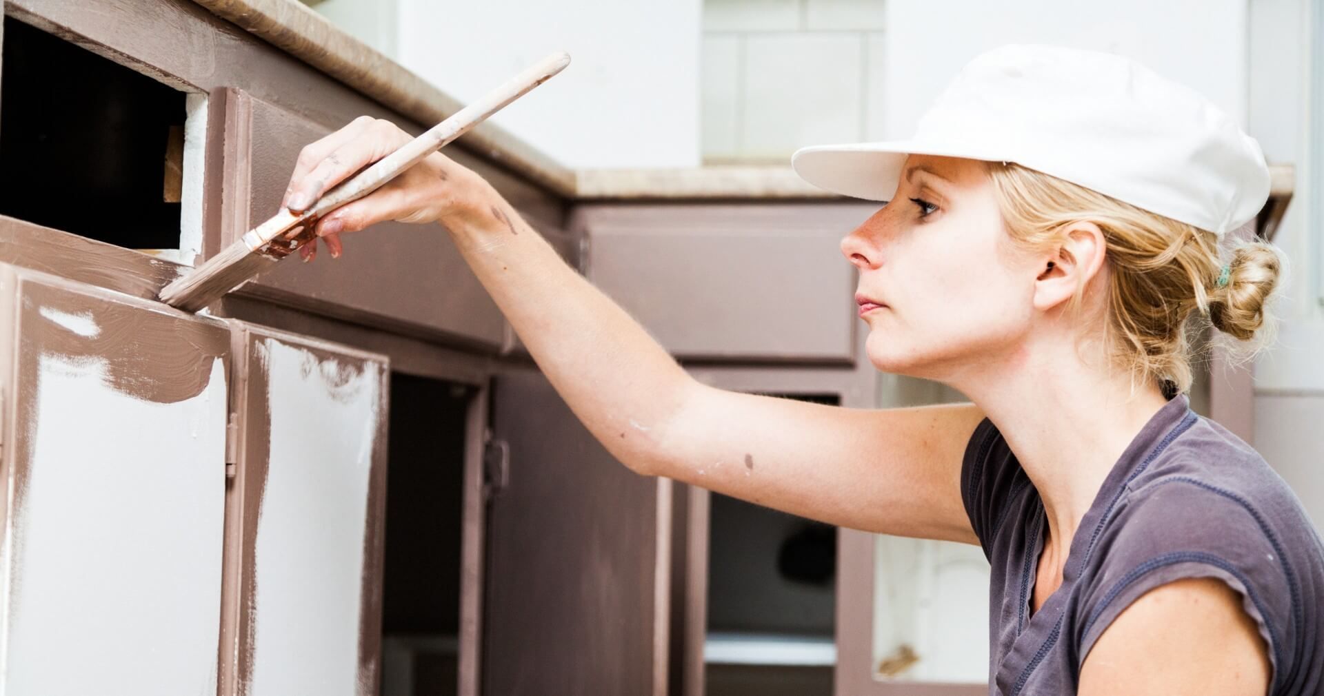 A woman painting her kitchen cabinets to give her kitchen a newer and fresher look