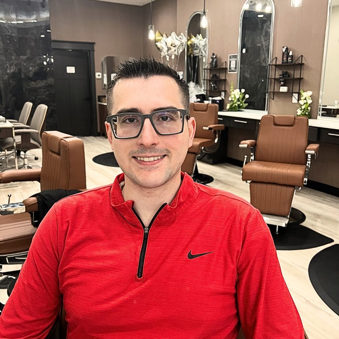 A man wearing glasses and a red shirt is sitting in a barber shop.