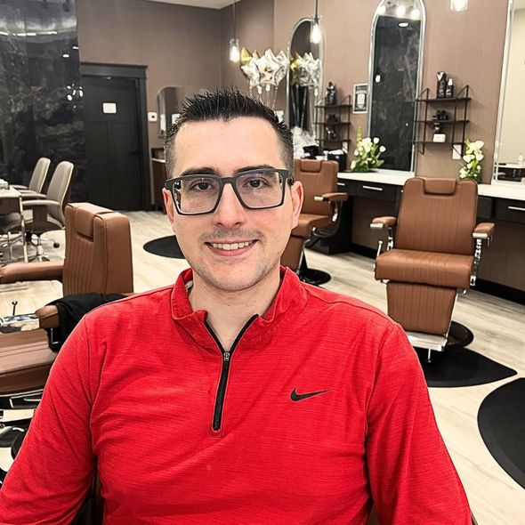 A man wearing glasses and a red shirt is sitting in a barber shop.