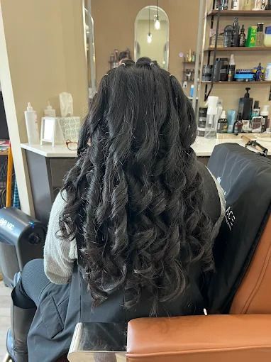 Woman with long, black, curled hair, seated in a salon chair.