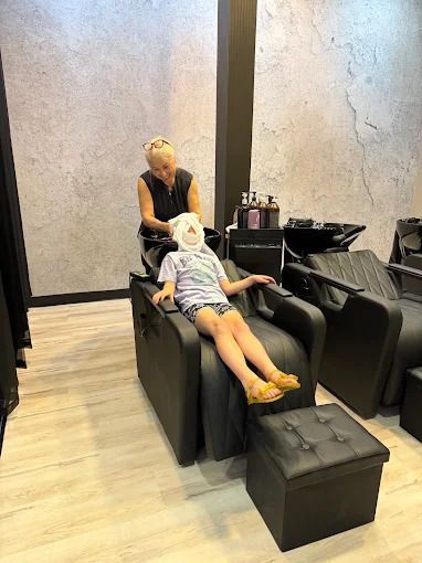 A person washing a child's hair at a salon. The child is reclined in a chair, receiving a hair wash.