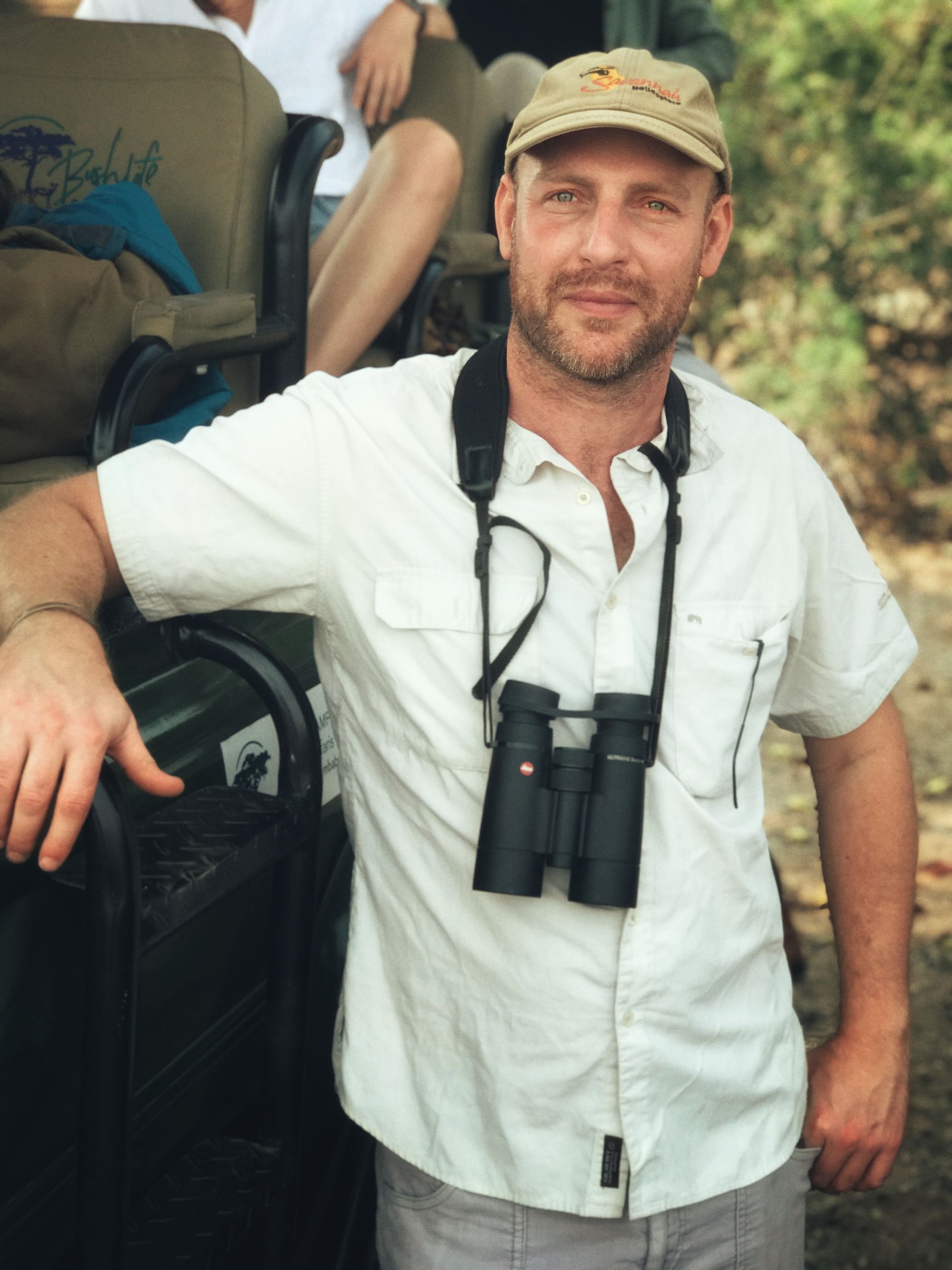 Woman in brown turtleneck, arms crossed, outside with bare trees in background.