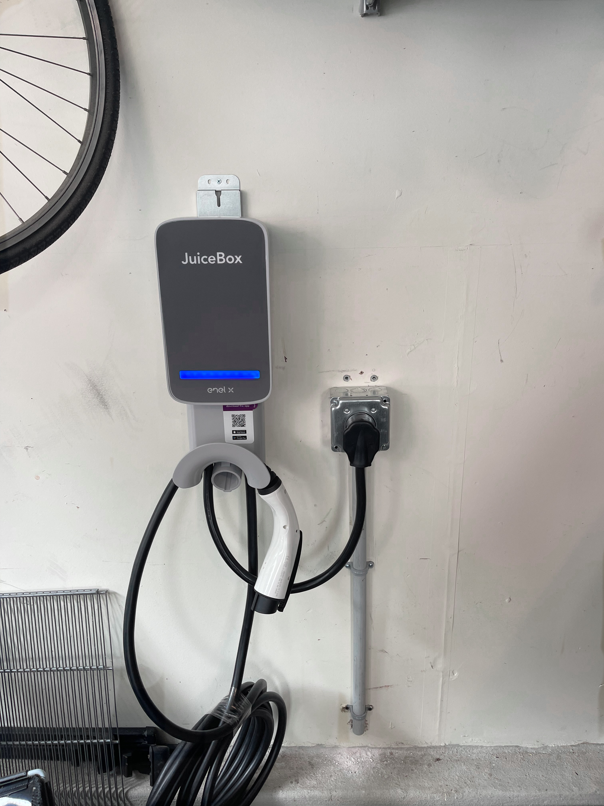 Electric vehicle charger mounted on a white wall with a plug-in connection. The cable hangs down.