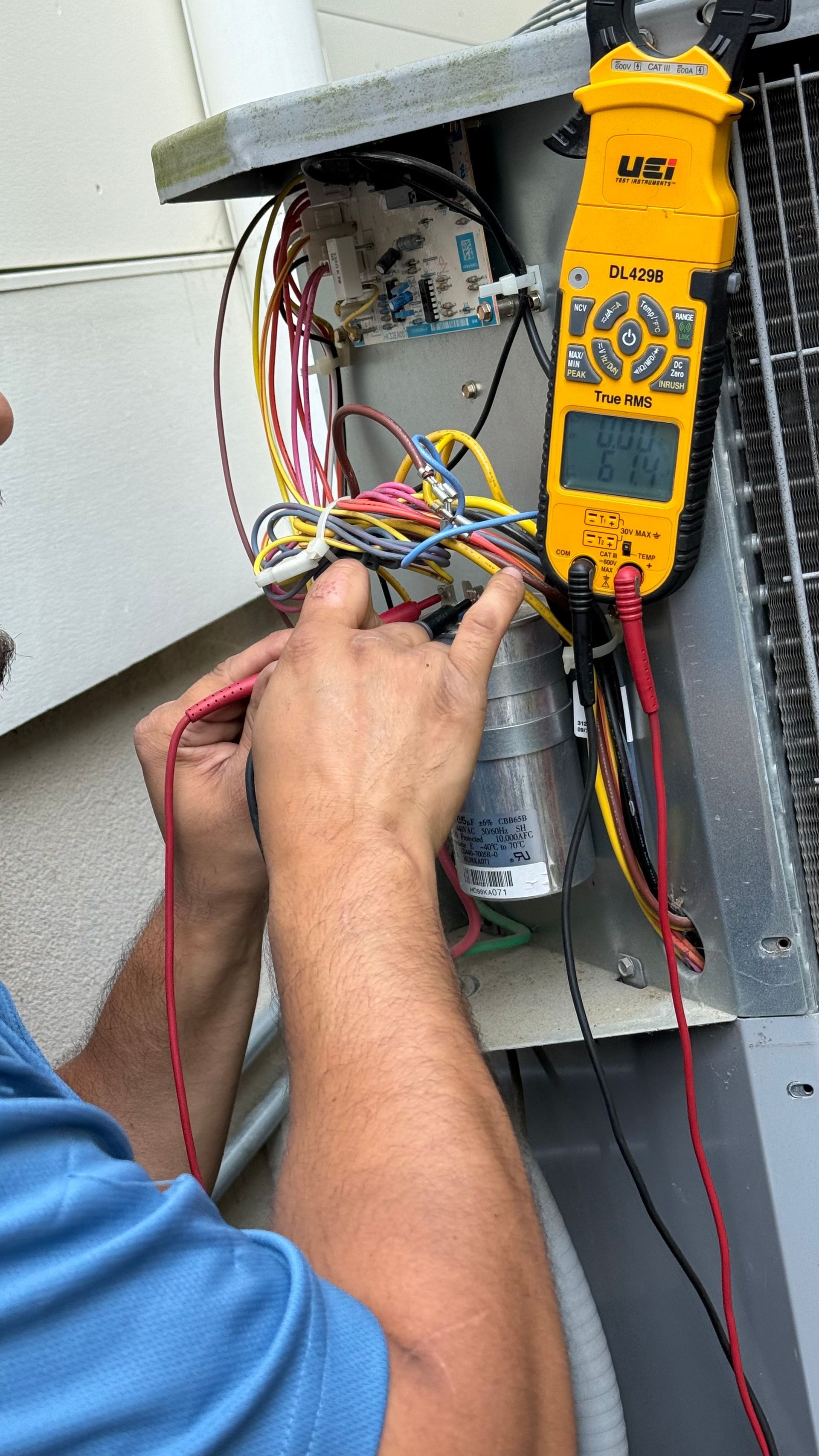 Person testing AC unit wires with a multimeter. Yellow meter attached; colorful wires.