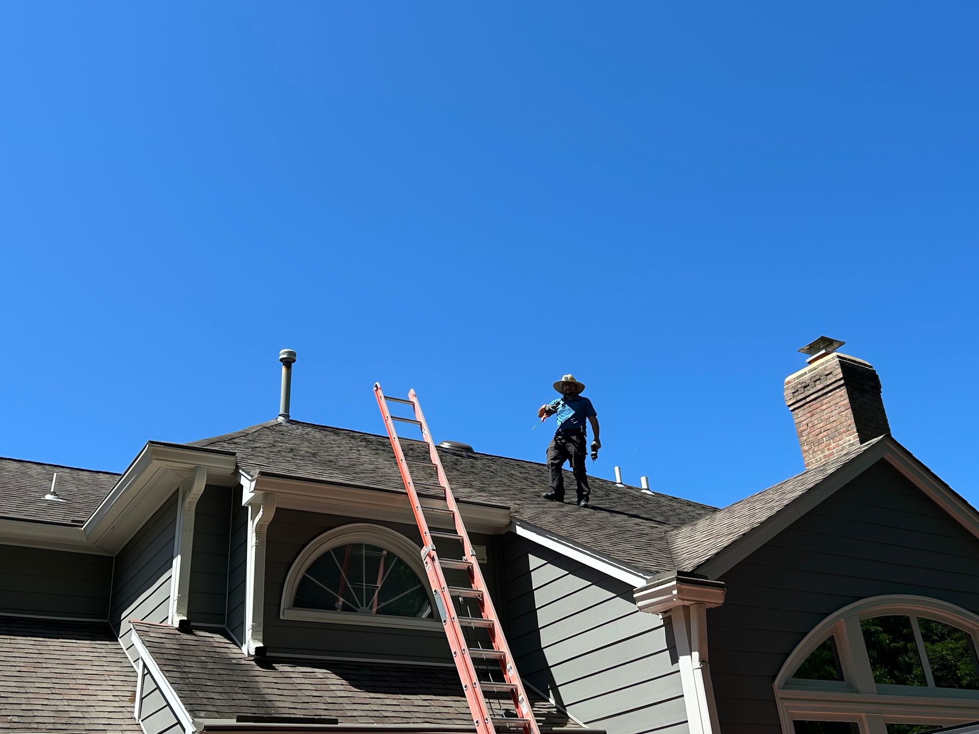 Person on a roof near a ladder under a clear blue sky.
