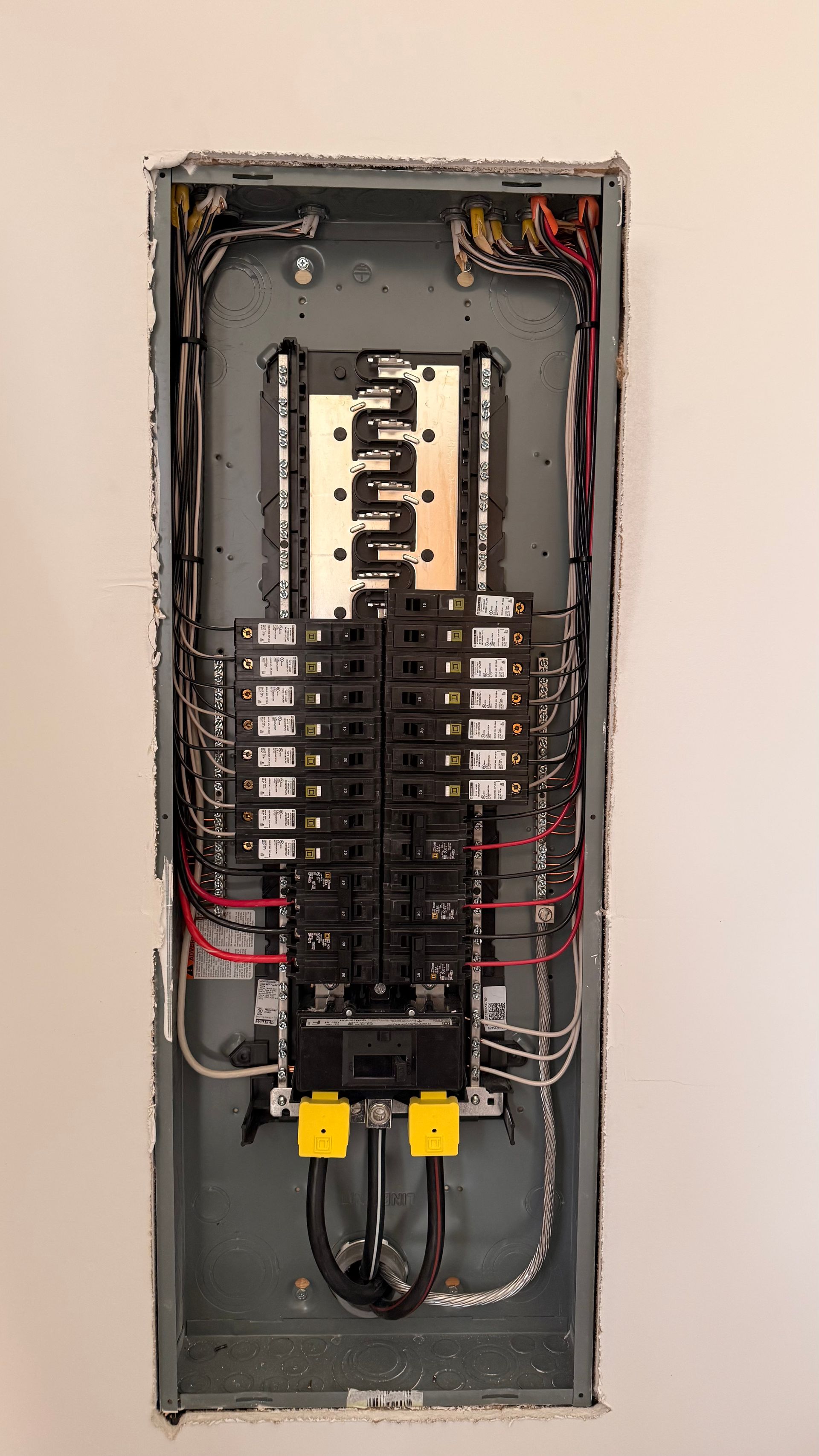 Electrical circuit breaker panel installed on a wall with multiple wires and breakers.
